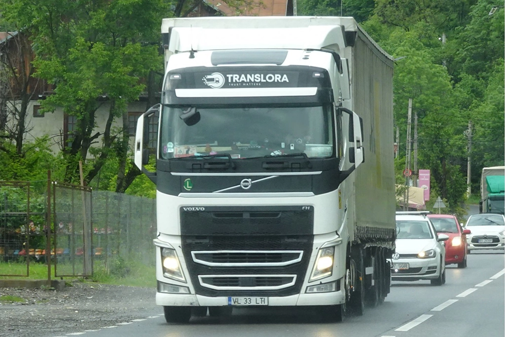 Camion Volvo alb si semiremorca cu prelata fotografiate in mers pe un drum national
